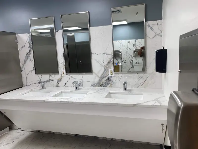 Three-sink marble vanity with new mirrors and stainless stall partitions in a commercial restroom