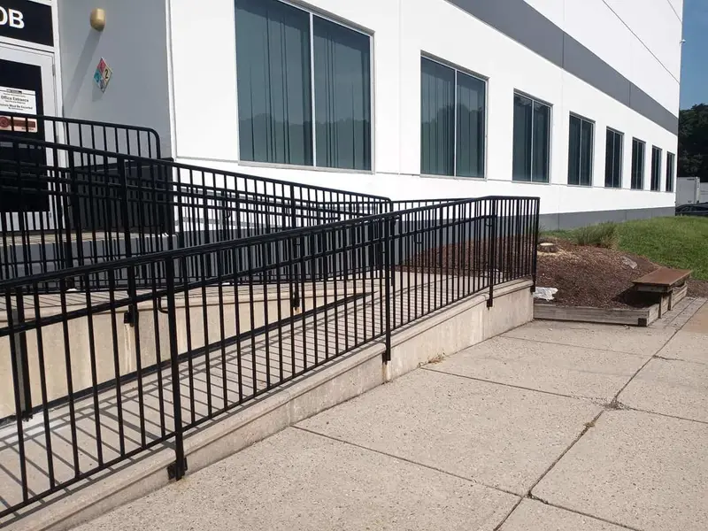 Black metal handrail along a new concrete accessibility ramp beside office windows
