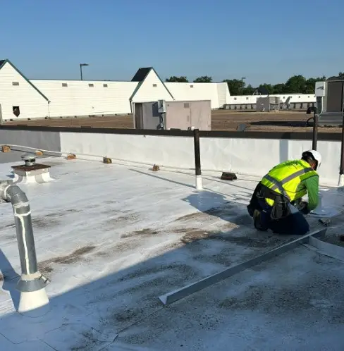 Roofing technician in a safety vest installing edge metal on a new TPO roof