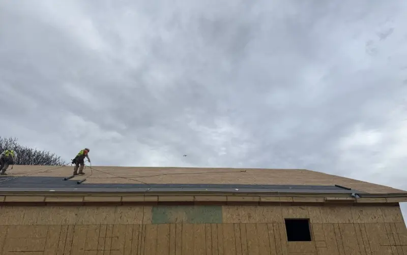 Crew installing synthetic underlayment on a new sloped roof deck