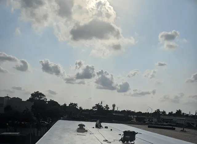 Roofing technician installing white TPO membrane on a commercial roof